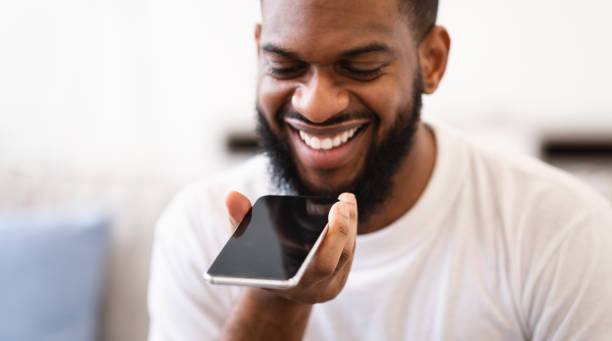 istock African Guy With Phone Using Voice Assistant App Indoors, Closeup 1305327446