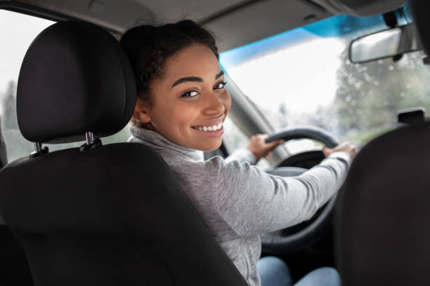 Cute driver, auto blogger and traveling with friends Cute driver, auto blogger and traveling with friends. Smiling beautiful young african american female turns to back seat and talk with passenger or client, view of window with raindrops, copy space black taxi stock pictures, royalty-free photos & images