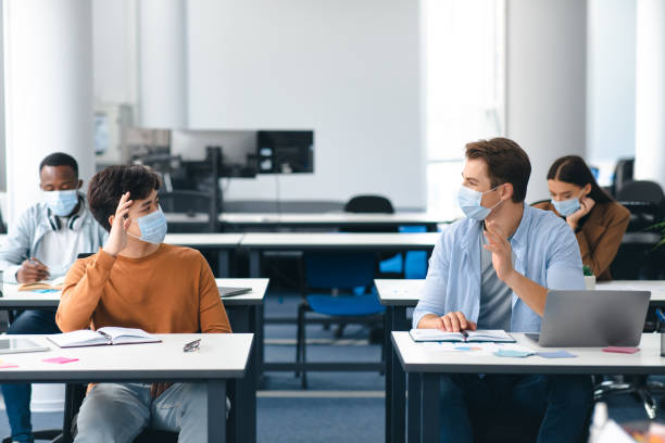 istock Diverse students wearing face masks greeting and waving 1305329397