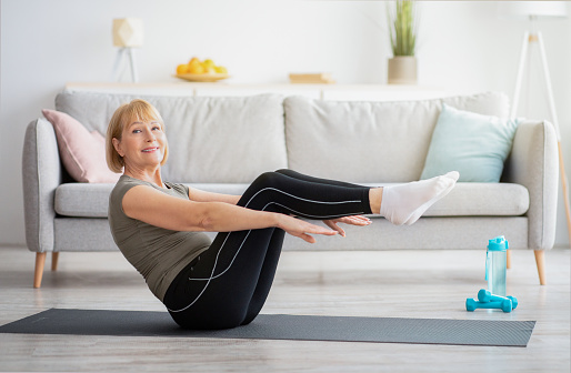 Happy senior woman doing abs exercises on yoga mat at home. Positive mature lady working out her core muscles, doing domestic fitness at living room. Stay fit and healthy during covid quarantine