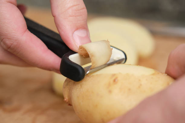 Closeup of man hands peeling a potato with a swiss vegetable peeler. Ingredient preparation concept. stock photo