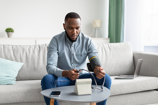 Hombre africano que mide presión arterial arterial sentado en casa photo