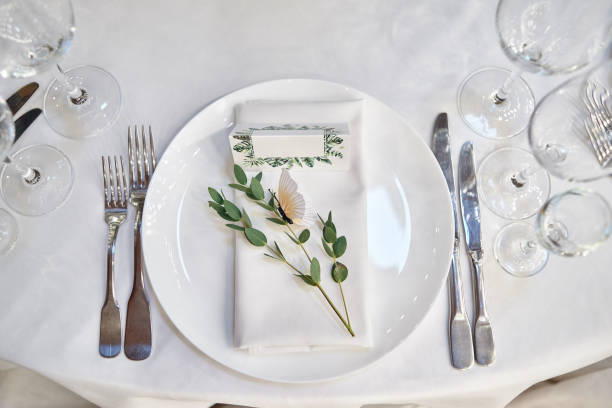istock Table setting with blank guest card on empty white plate and cutlery on table, copy space. Menu mockup, place setting at wedding reception. Table served for wedding banquet in restauran 1305332643