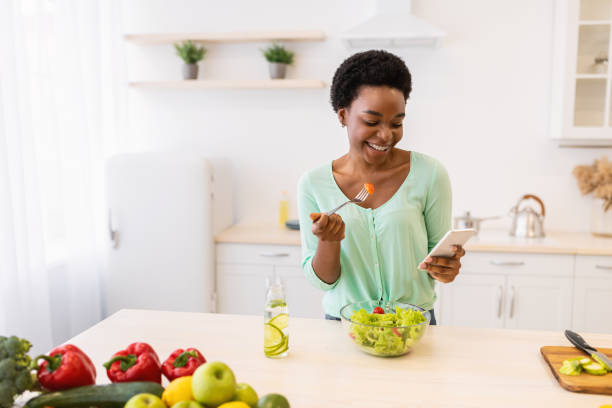 istock Black Woman Using Smartphone Eating Vegetable Salad In Modern Kitchen 1305333474