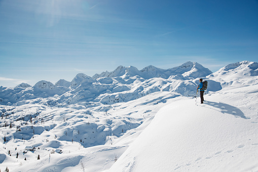 One man only, lonely winter mountaineer, hiker going up the snowy mountain, clear skies on a sunny winter day and perfect weather conditions in the European Alps. Snow caped mountains glistening in the sun.