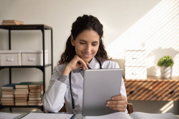 istock Close up smiling female doctor using tablet, watching webinar 1305333561