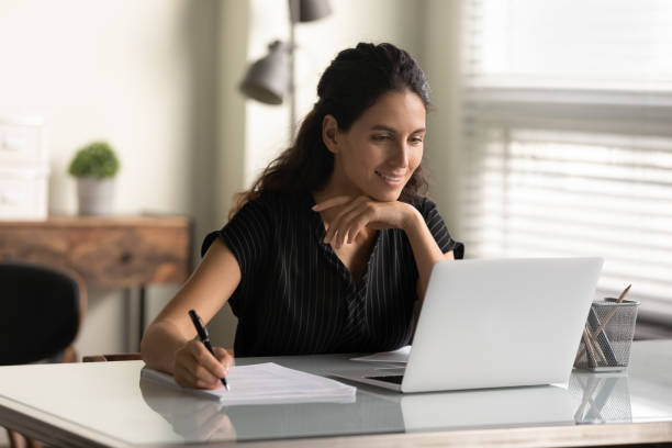 istock Smiling woman looking at laptop screen, taking notes, studying online 1305333604