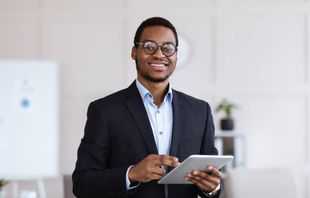 Cheerful black man manager holding digital tablet, office interior Cheerful young black man manager in glasses holding digital tablet and smiling at camera, office interior, copy space. African american businessman using business application on pad recruiter stock pictures, royalty-free photos & images