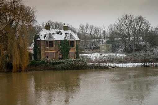 Derelict house on the River Great Ouse during a snow shower, It has holes in the roof and has been uninhabited for several years.