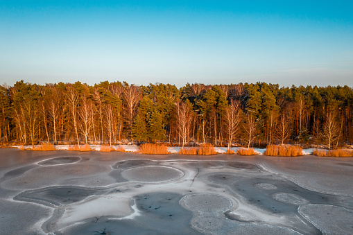 Aerial view of the shore of the frozen lake in winter in the light of the setting sun.
