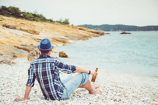 Young Caucasian man sitting at the beach alone.