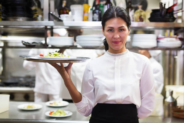 istock Successful waitress standing in restaurant kitchen with ordered meals 1305338144