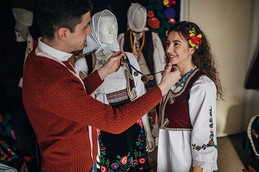 Two people, male tailor for Serbian national costumes in his workshop, with a woman who came to try on custom made clothes just for her.