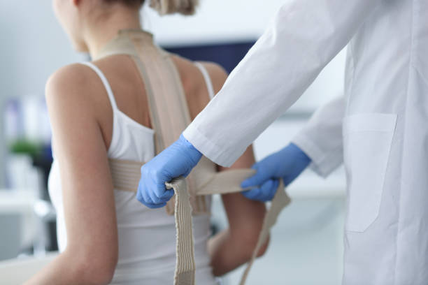 doctor putting corset on back of female patient closeup - bustiers imagens e fotografias de stock