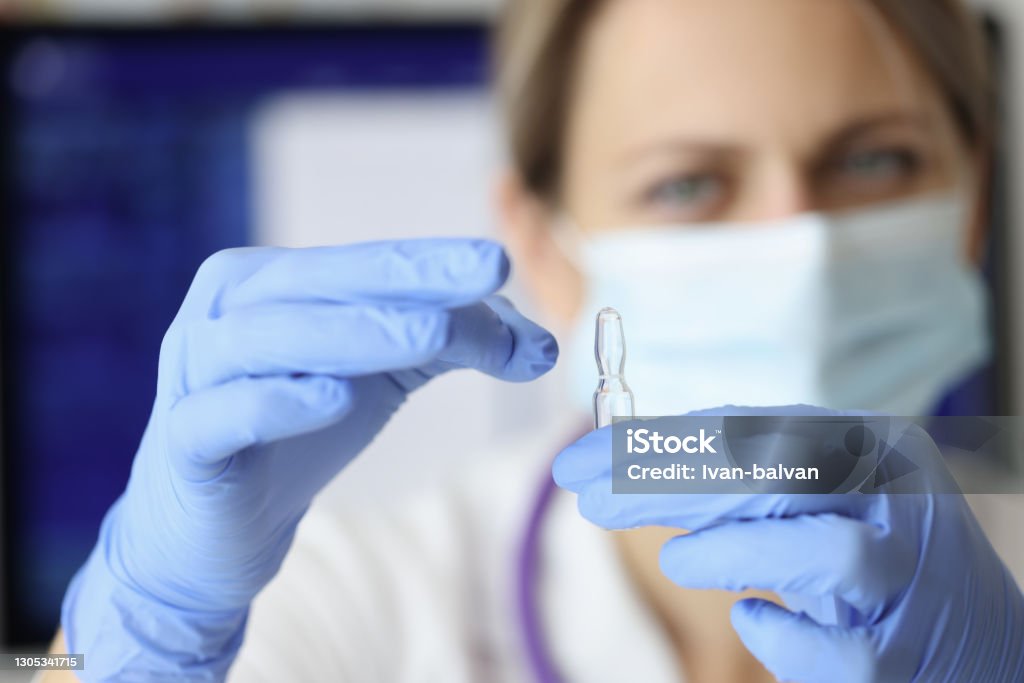 Nurse in mask and gloves holding ampoule of medicine closeup Nurse in mask and gloves holding ampoule of medicine closeup. Parenteral drug administration concept Ampoule Stock Photo