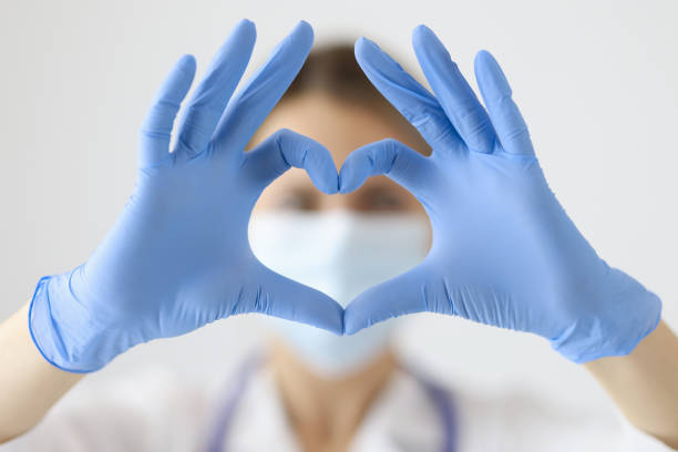 medico in maschera protettiva che mostra il cuore con le mani da vicino - glove surgical glove human hand protective glove foto e immagini stock
