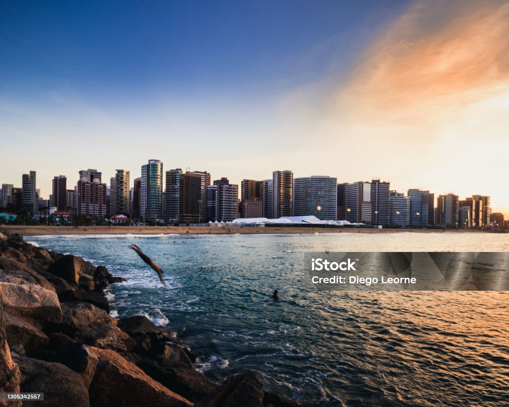 Man diving into Iracema Beach during sunset Man jumping from a sea breaker into the sea with city buildings in the background Fortaleza - Ceará State Stock Photo