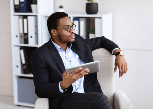 istock Thoughtful black businessman sitting in chair, using digital tablet 1305342563