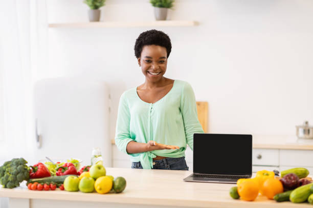 istock Black Woman Showing Laptop Screen Posing In Kitchen At Home 1305343083