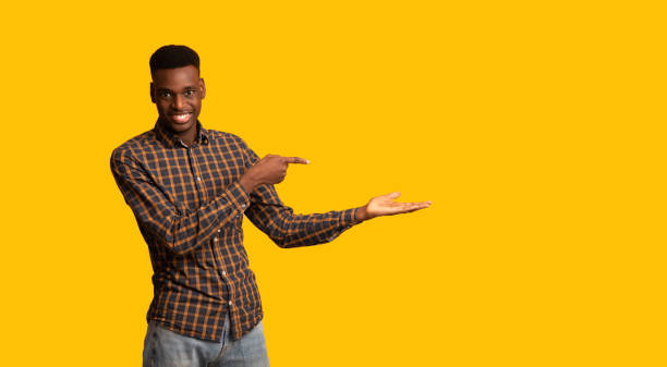 istock Cheerful Black Guy Pointing Finger At Open Palm, Isolated On Yellow Background 1305343378