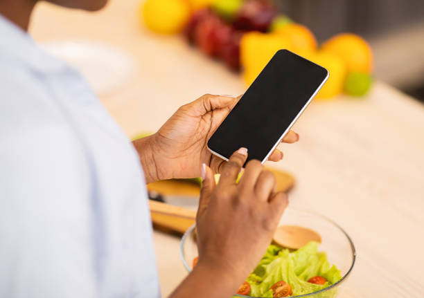 istock Black Woman Using Phone With Blank Screen In Kitchen, Cropped 1305344437