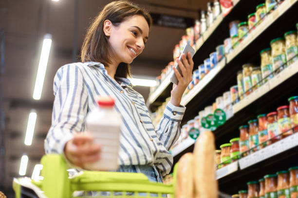 istock Female customer holding smartphone standing in store taking products 1305344674