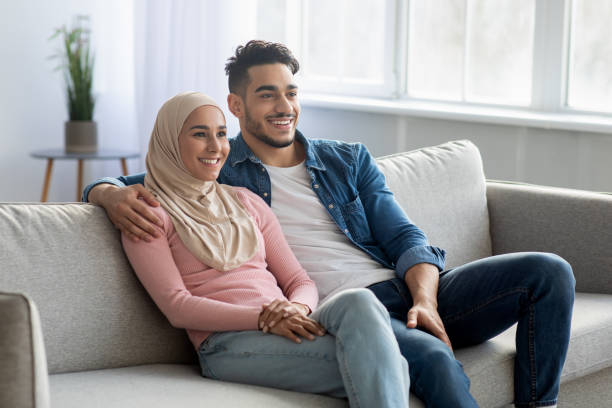 istock Cheerful muslim couple sitting on couch at home, copy space 1305344707