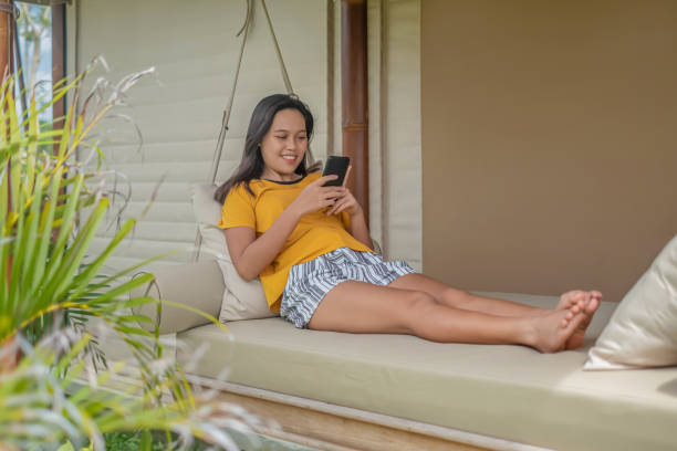 istock Young Southeast Asian Woman Text Messaging on a Hanging Daybed 1305345659