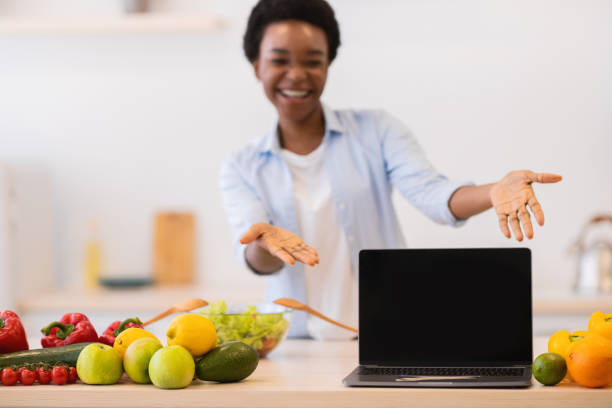 istock Black Lady Showing Laptop With Blank Screen In Kitchen, Mockup 1305345875
