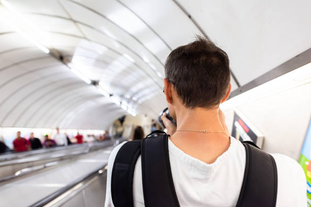 london, uk man back riding escalator down standing in underground tube metro during morning commute in center of downtown city - canary wharf railway station imagens e fotografias de stock