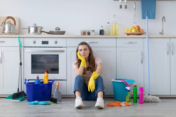 esausta giovane casalinga seduta sul pavimento in cucina, circondata da prodotti per la pulizia, stanca dai lavori domestici - stereotypical homemaker foto e immagini stock