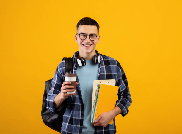 istock Happy male student with notebooks, backpack and takeaway coffee looking at camera and smiling on orange background 1305348078