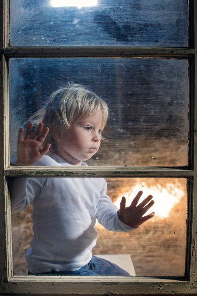 istock Blond child behind the window, looking outside 1305350709