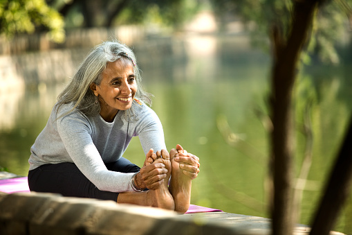 Senior woman practicing yoga pose by lake at park