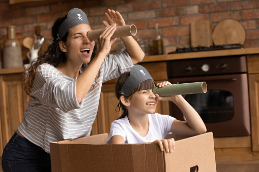 Overjoyed young Hispanic mother and little 7s daughter have fun playing pirates game at home together. Playful happy Latino mom or nanny and small girl child engaged in funny activity on weekend.