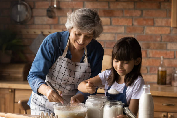 Happy senior grandmother and small granddaughter bake at home Smiling mature Hispanic granny and small granddaughter work with flour bake cookies in kitchen at home. Happy caring senior grandmother and little grandchild cook breakfast or dessert together. spanish breakfast stock pictures, royalty-free photos & images