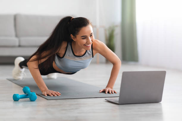istock Athletic young woman exercising in living room, using laptop 1305351299