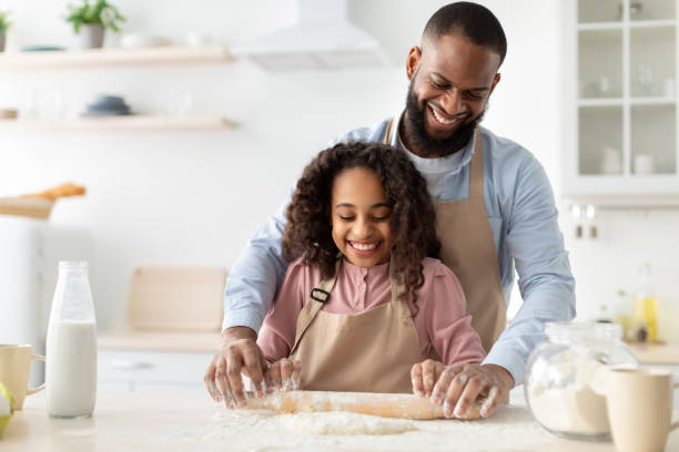 счастливый черный человек и его дочь ребенка свертывая тесто - свертывая стоковые фото и изображения