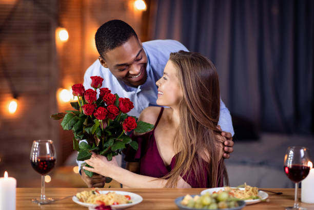 type afro-américain affectueux surprenant sa belle amie avec le bouquet de roses - anniversary couple rose black photos et images de collection