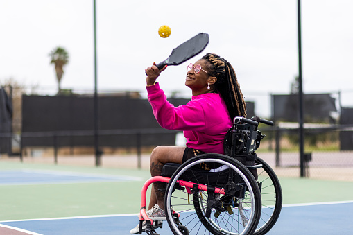 A young black disabled woman playing pickleball with her friend.