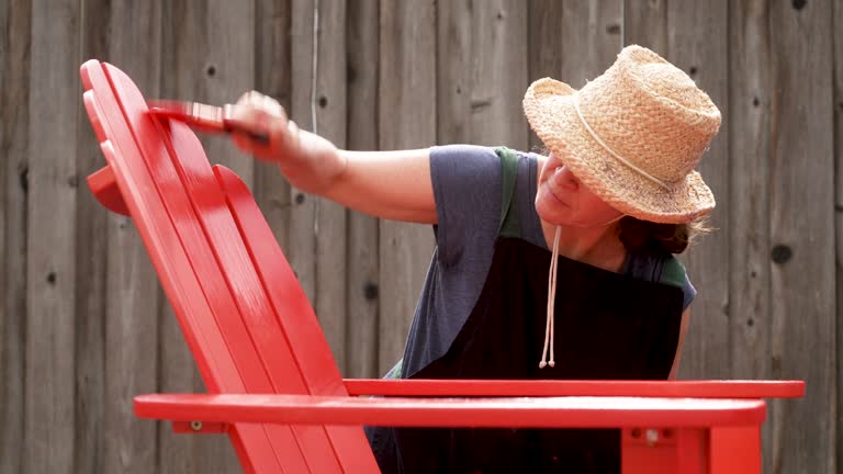 Mature woman painting a beach chair at her backyard