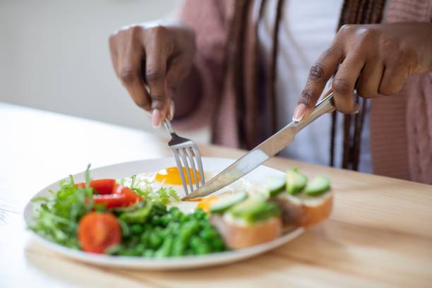istock Unrecognizable african woman eating tasty breakfast in kitchen, using fork and knife 1305354352