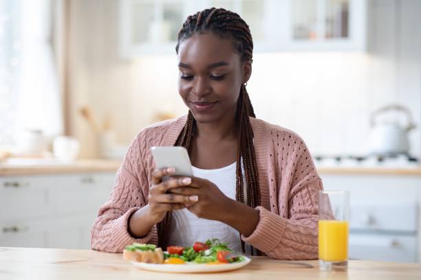 istock Smiling Black Woman Texting On Smartphone While Having Breakfast In Kitchen 1305354373