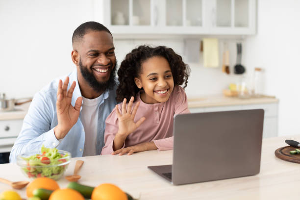 istock Black man and girl having videocall using laptop waving hands 1305355591