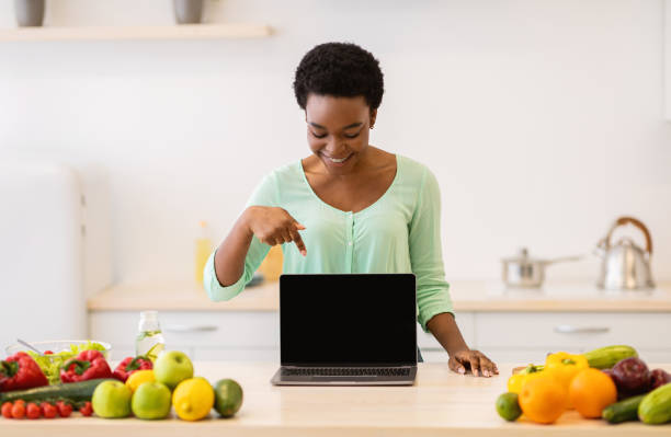 istock African female showing laptop empty screen standing in kitchen indoors 1305355735