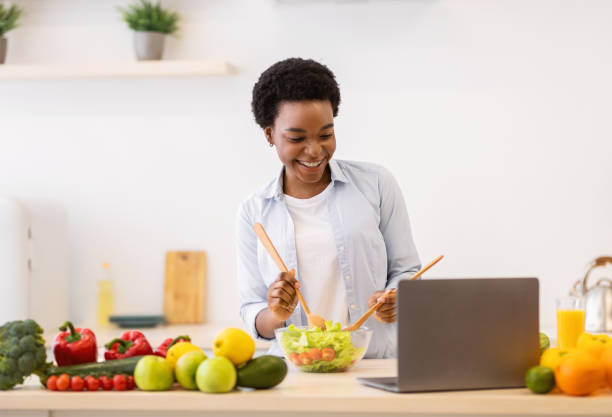 istock Black Lady Cooking And Using Laptop Preparing Salad In Kitchen 1305355794