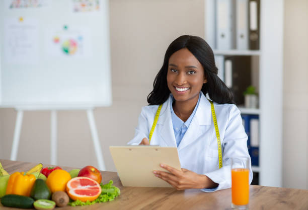 istock Young black nutritionist with clipboard creating plant based meal plan for patient at weight loss clinic, free space 1305356562