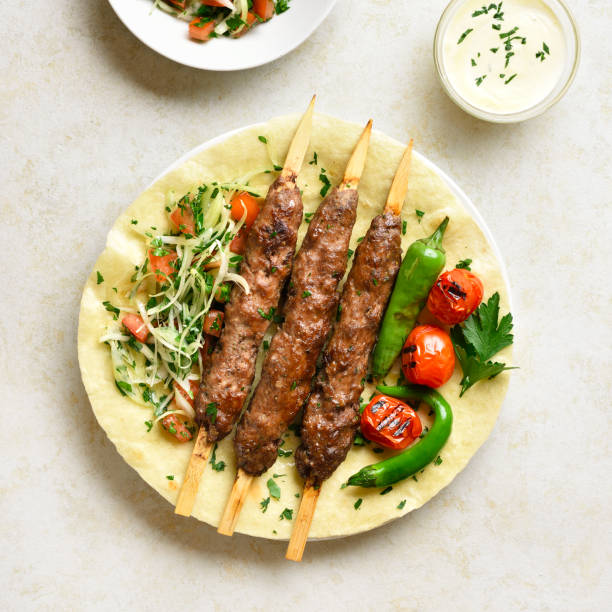 Turkish Adana Kebab with fresh vegetables Close up view of turkish Adana Kebab with fresh vegetables on flatbread over light stone background. Top view, flat lay shish kebab stock pictures, royalty-free photos & images