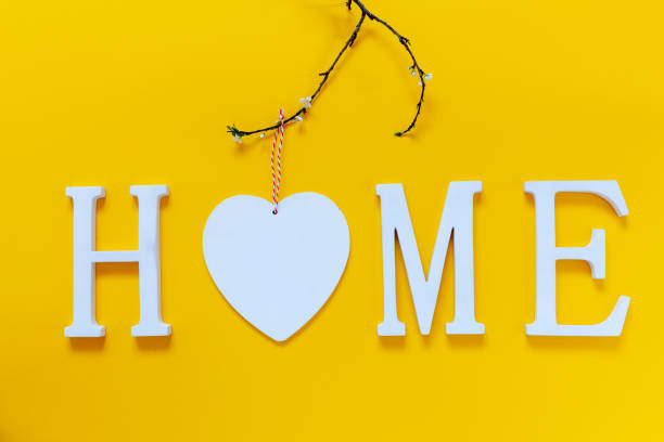 Home, wooden text with heart shape decor on yellow background. Concept of building houses, choosing your own house, mortgage, buying, selling residential area, rental, insurance, investment real estate. casa, texto de madera con decoración en forma de corazón sobre fondo amarillo. concepto de construcción de viviendas, elección de su propia casa, hipoteca, compra, venta de zona residencial, alquiler, seguros, inmobiliarias de inversión.