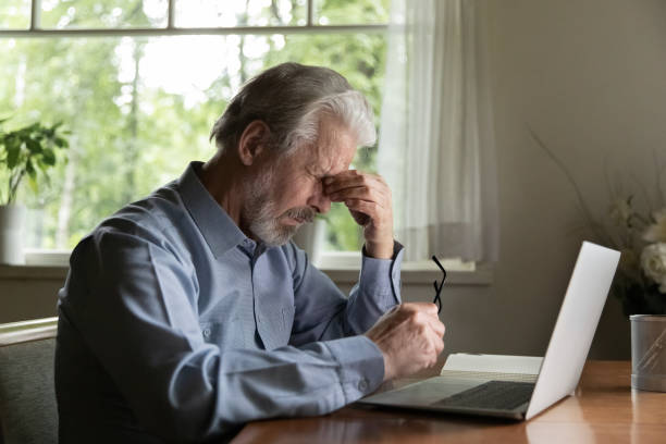 müde reifen 60er jahre mann arbeitet am laptop von zu hause - human eye rubbing tired glasses stock-fotos und bilder